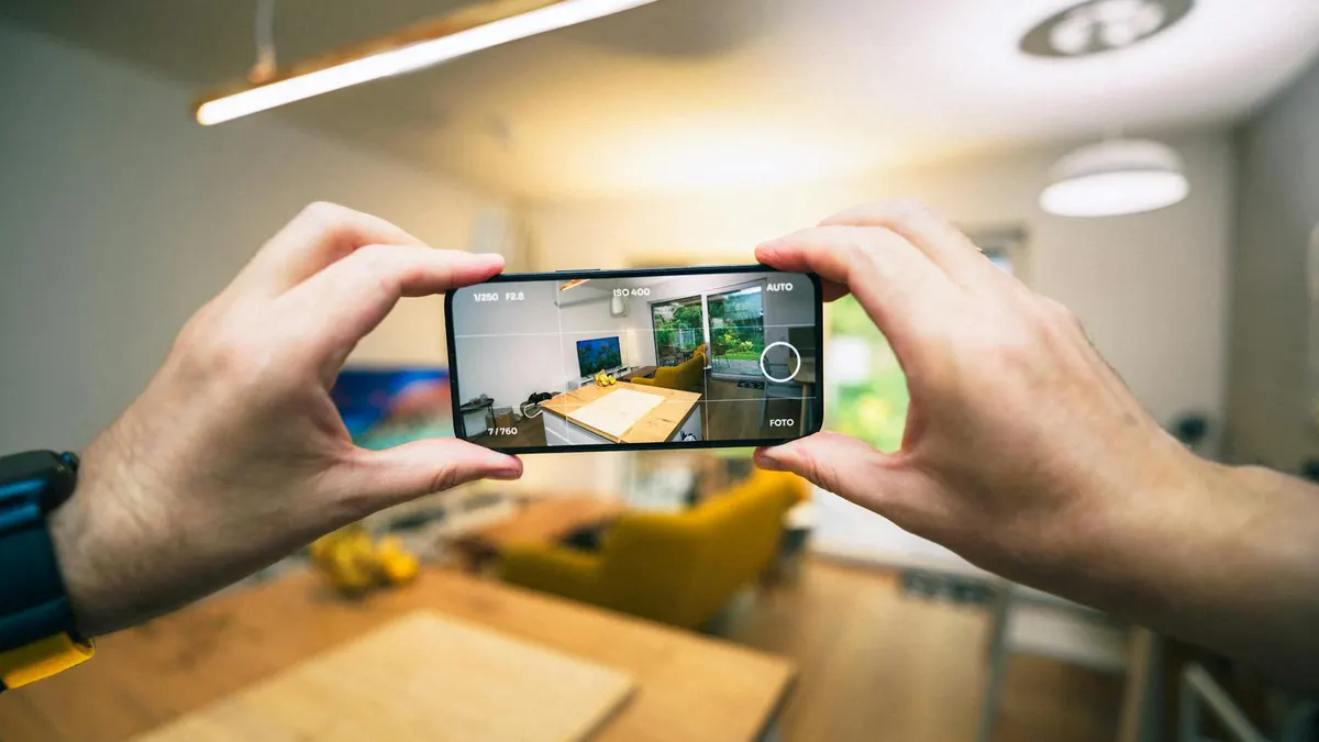 Mani che inquadrano un soggiorno con lo smartphone per fotografarlo